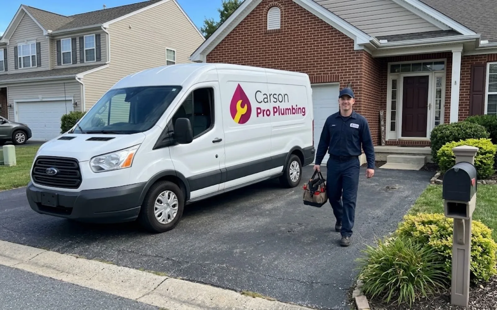 Carson Pro Plumbing service van parked in a residential driveway with a technician carrying a tool bag